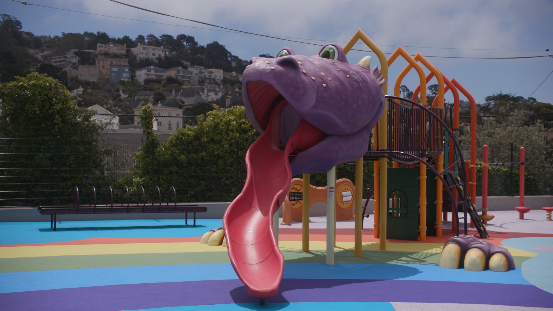 Purple dragon head play structure with red tongue slide rainbow safety surfacing