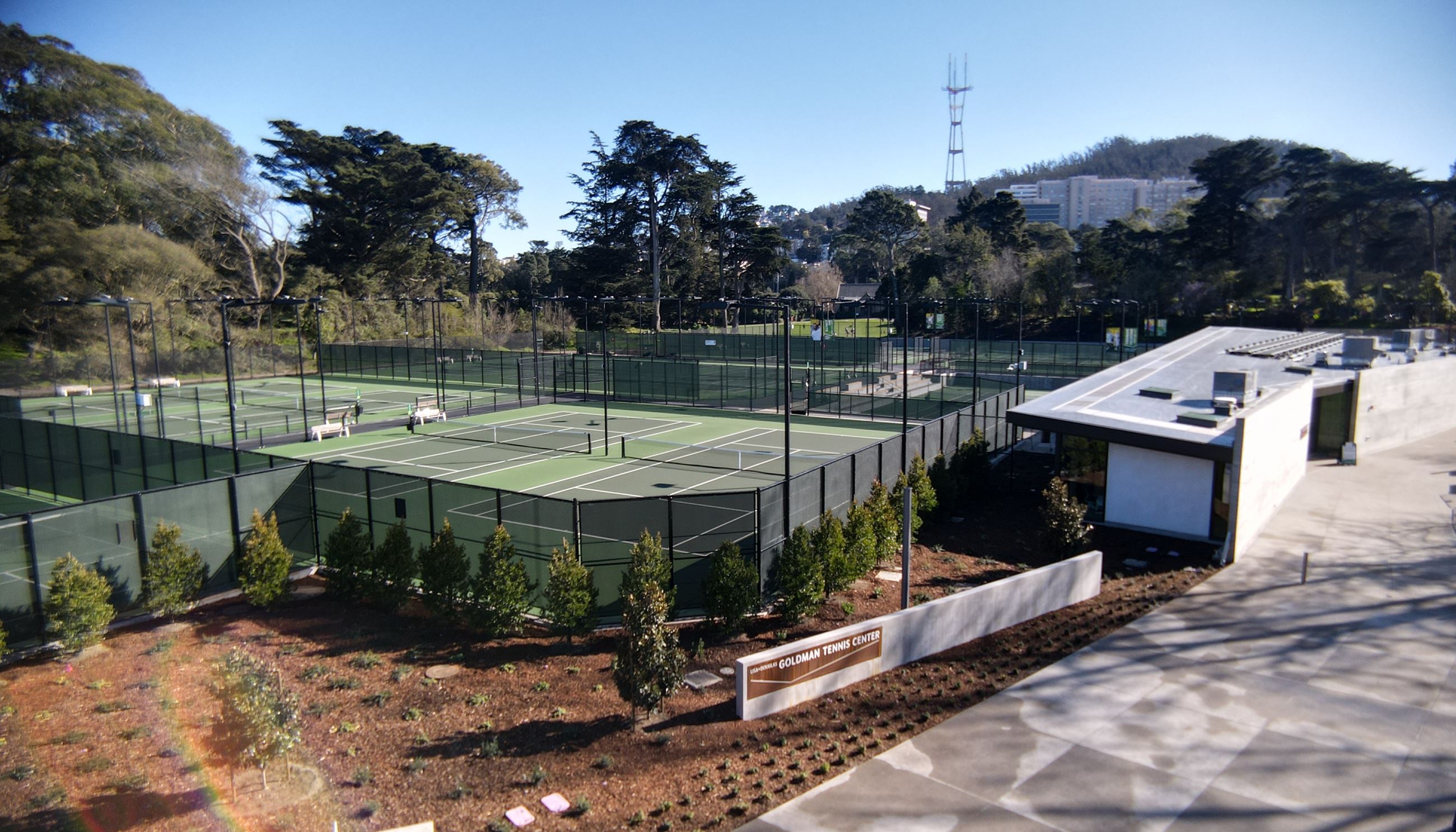 View from the back of the tennis center clubhouse. Planter bed in front of two of the courts. Opens in new window