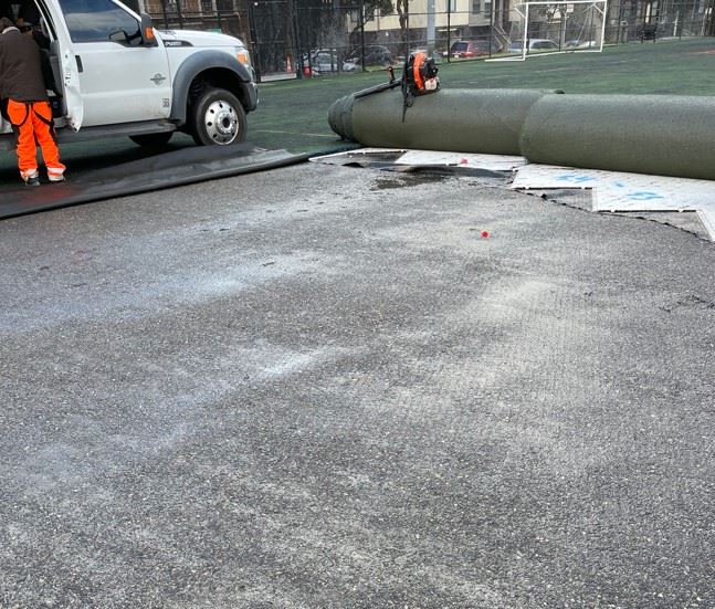 Crews pull back existing artificial turf to test base material drainage